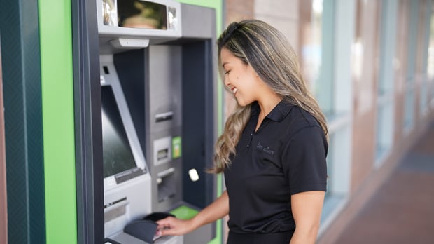 A woman wearing a black shirt uses an automated teller machine.